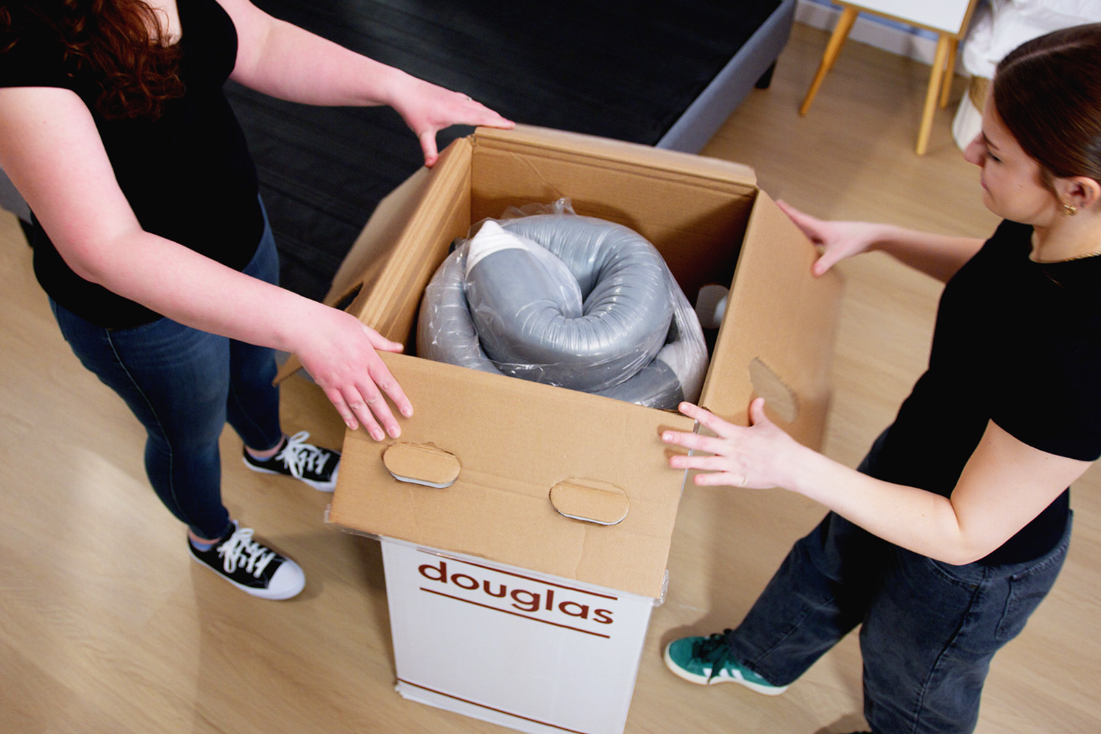 Two people opening up a boxed mattress in a bedroom