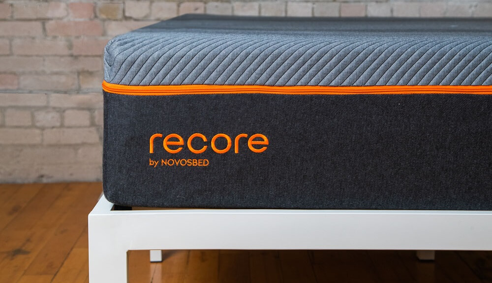 Image of the orange logo on the Recore mattress, sitting on a white bed frame.