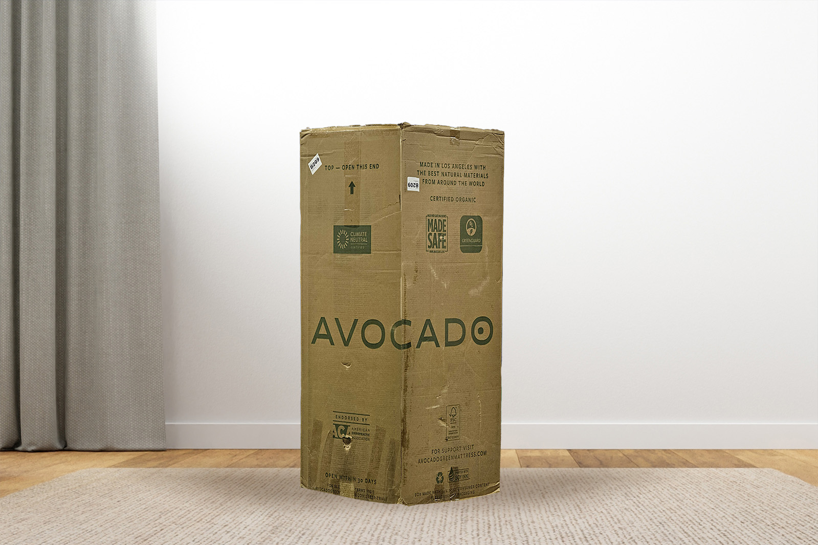 AvocadoGreenBox MattressReviewscom Photo of the Avocado Green mattress box on the floor in a bedroom taken from a front angle