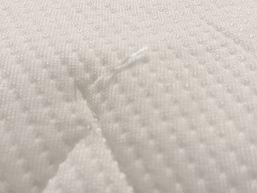 White cover fabric of the Endy Hybrid mattress with loose thread in tufting