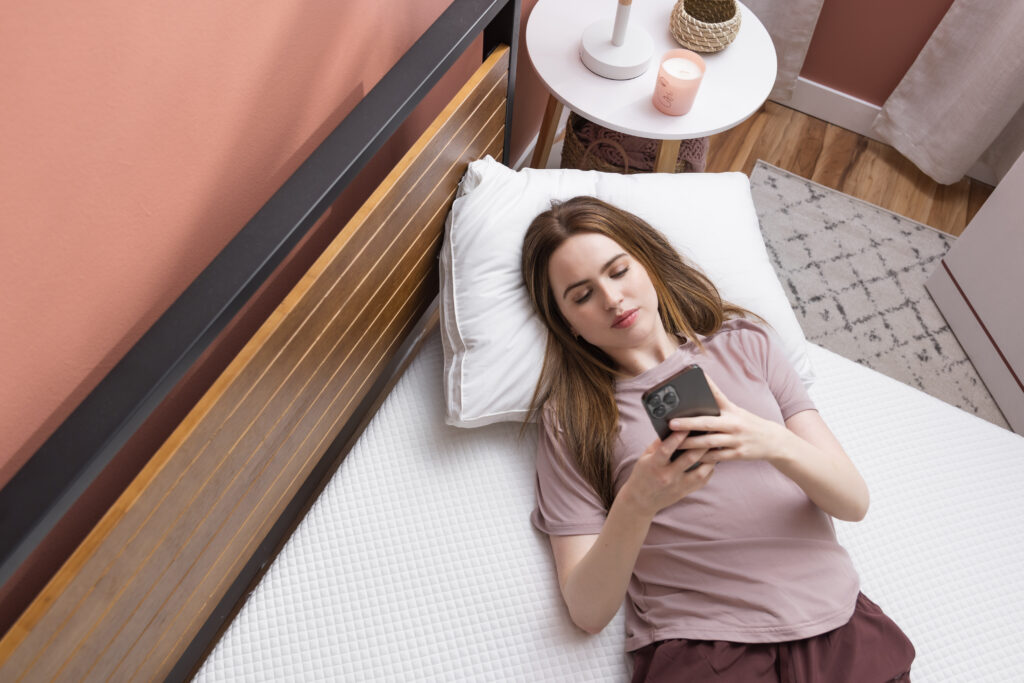 Young woman using a cell phone while laying on the Douglas mattress.