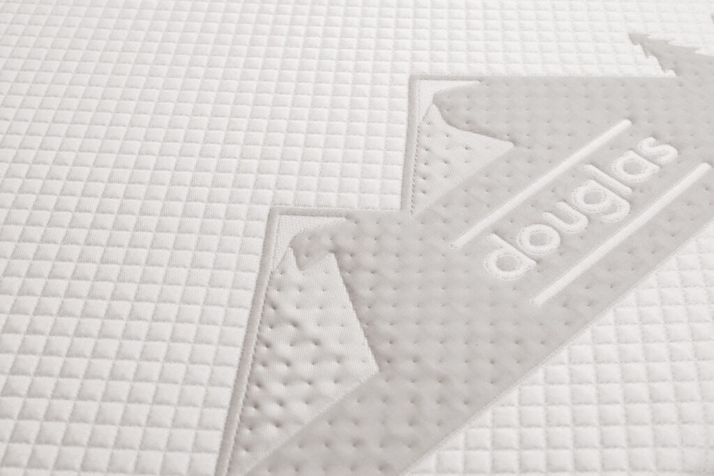 Closeup photo of the quilted white cover of the Douglas Summit mattress, including Douglas logo set in mountainscape