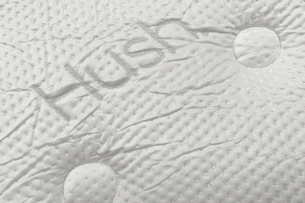 The wrinkly white fabric of the Hush mattress cover with HUSH logo sewn in