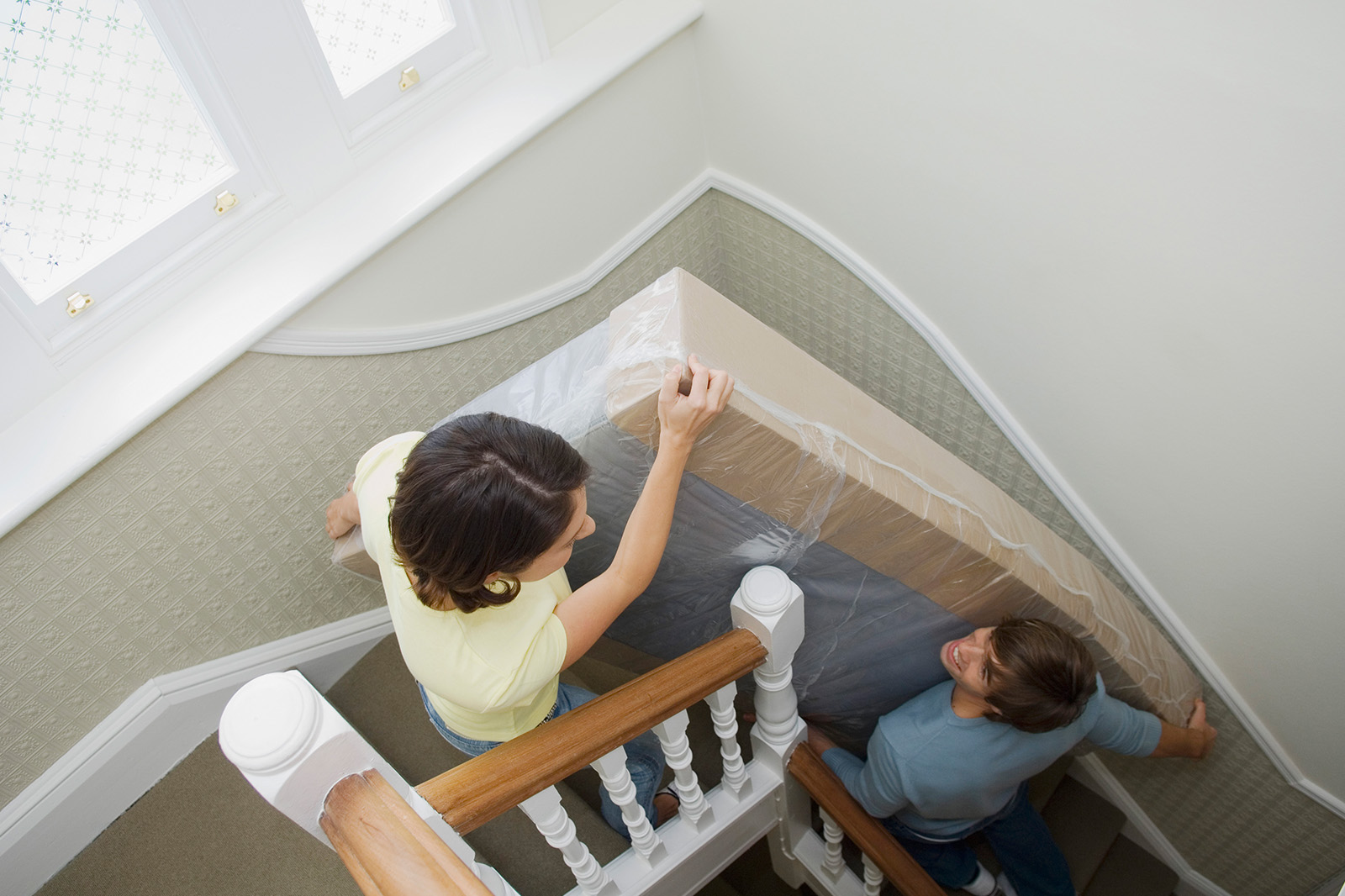 Image of two people moving their mattress up stairs in a house