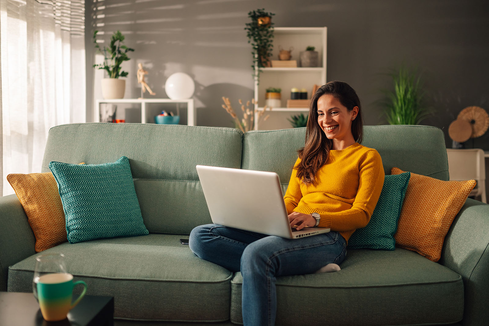 Women sitting on a green couch smiling at her laptop