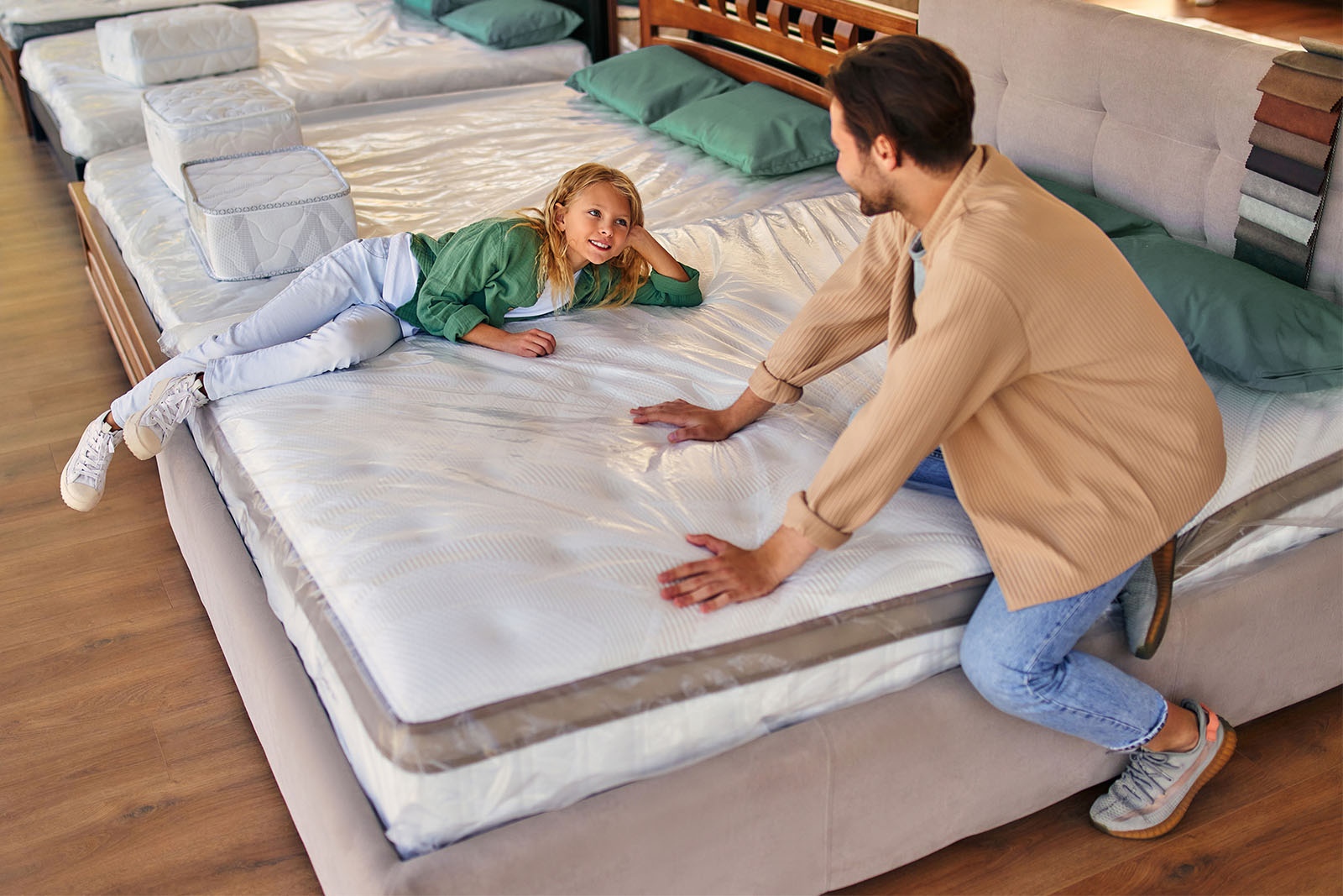 A father and his daughter at a mattress store lying down and pressing on the mattress