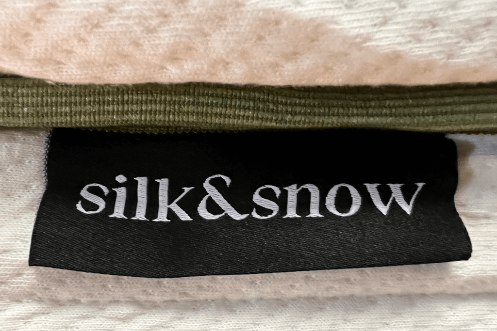 A close up of the Silk and Snow Organic Mattress tag with the company logo stitched underneath the green trim surrounding the mattress.