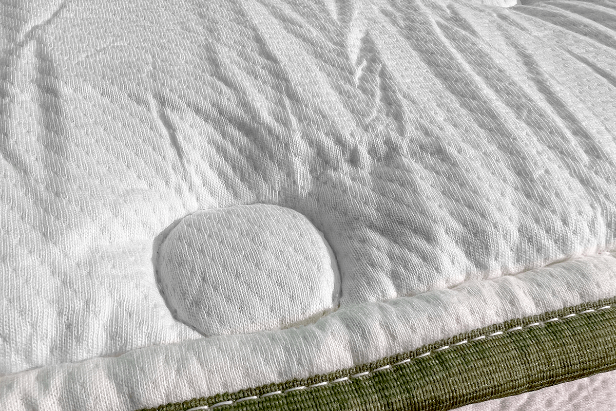 A close up of the Silk and Snow Organic Mattress cover with white, diamond shaped stitching and an olive green trim.