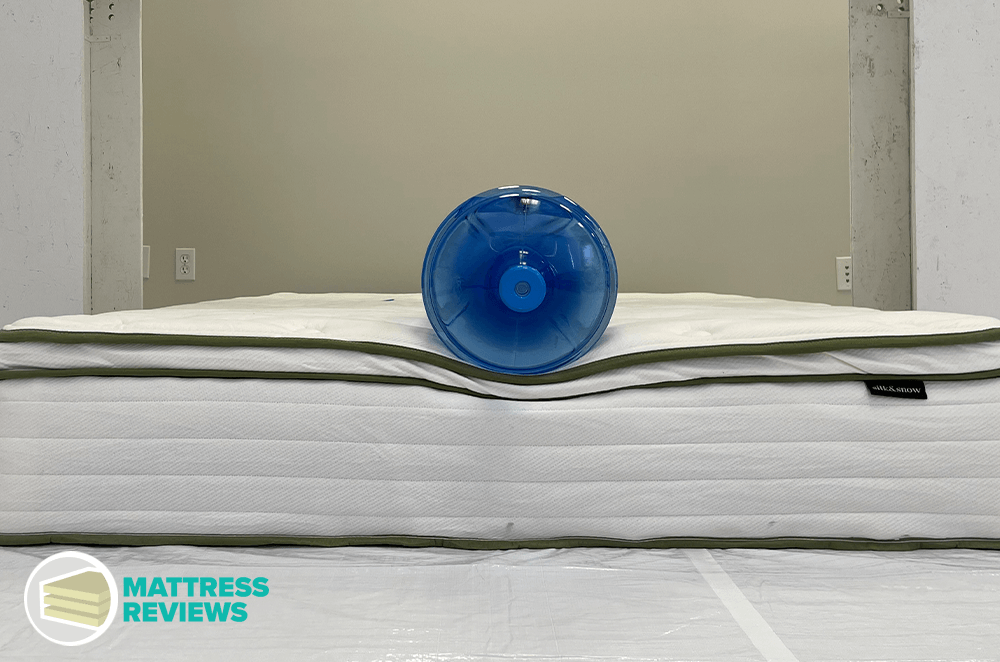 A large water jug sits on the top edge of the Silk and Snow Organic Mattress to test for edge support.