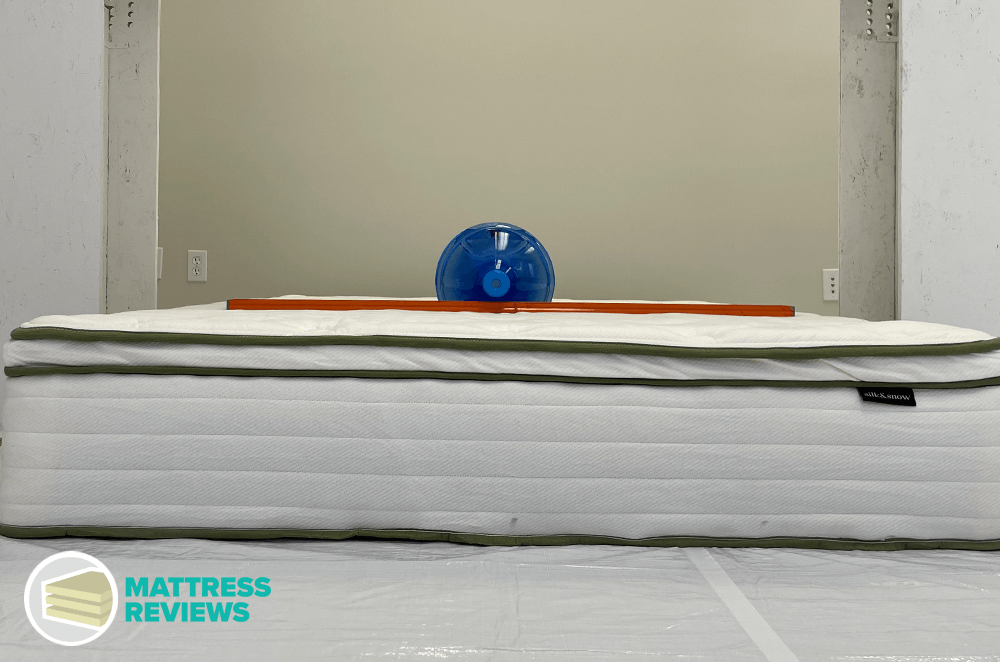 A large water jug and a level sit on top of a Silk and Snow Organic Mattress to test for firmness.