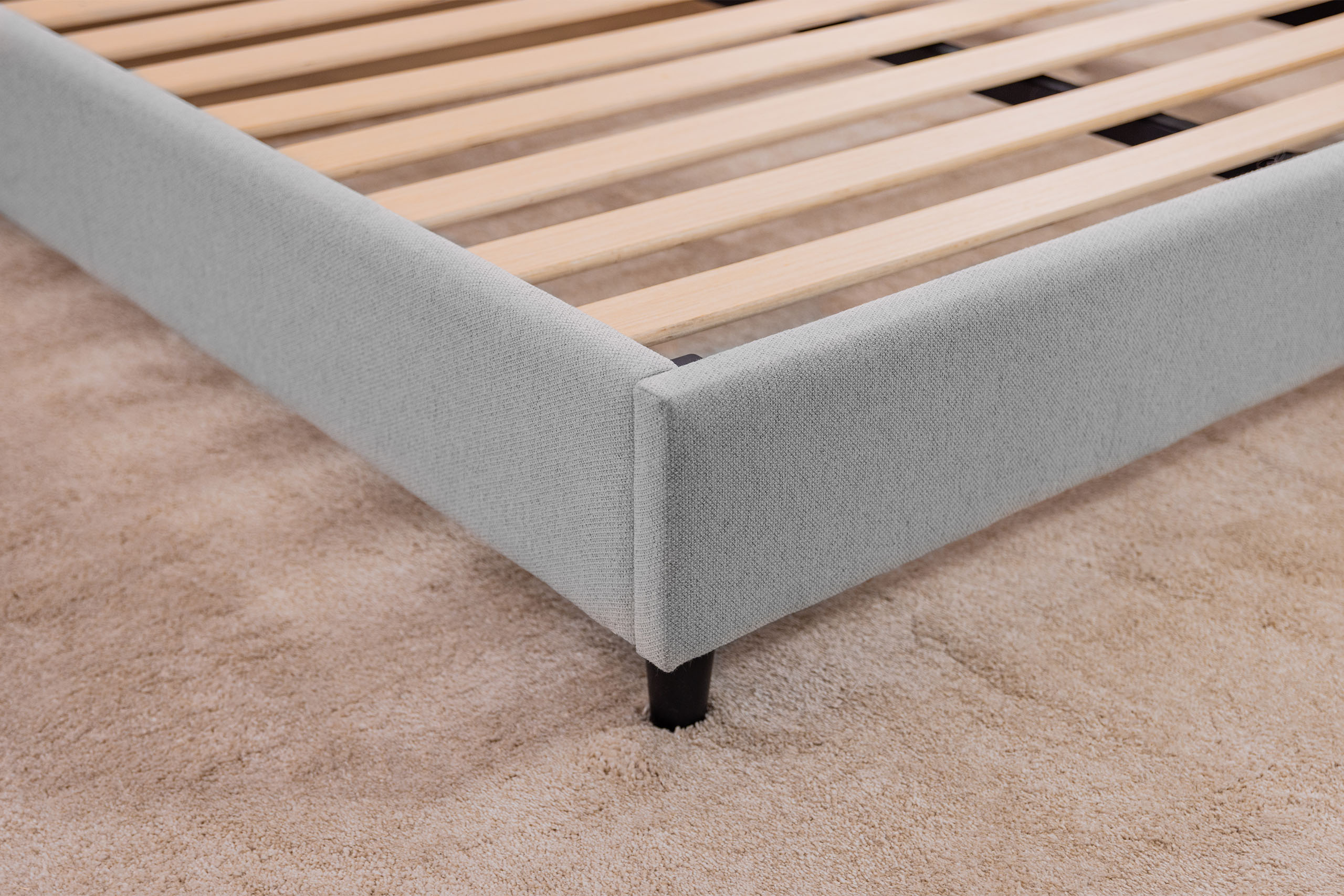 Corner view of the Logan & Cove upholstered bed frame without a mattress, showing its wooden slats.