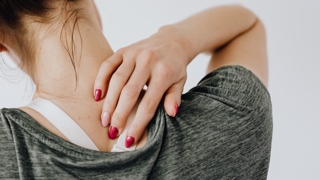 A woman in a grey shirt rubs her sore neck